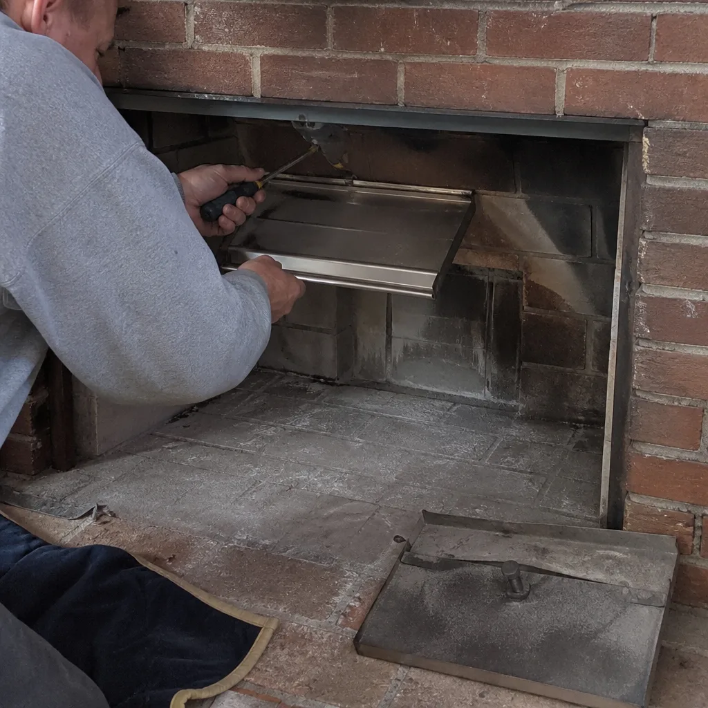 Technician installing a stainless steel fireplace damper plate